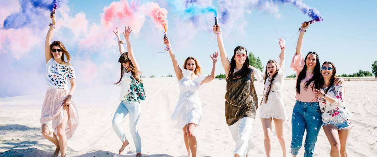 Bridesmaids holding colored smoke bombs for bachelorette party on the beach