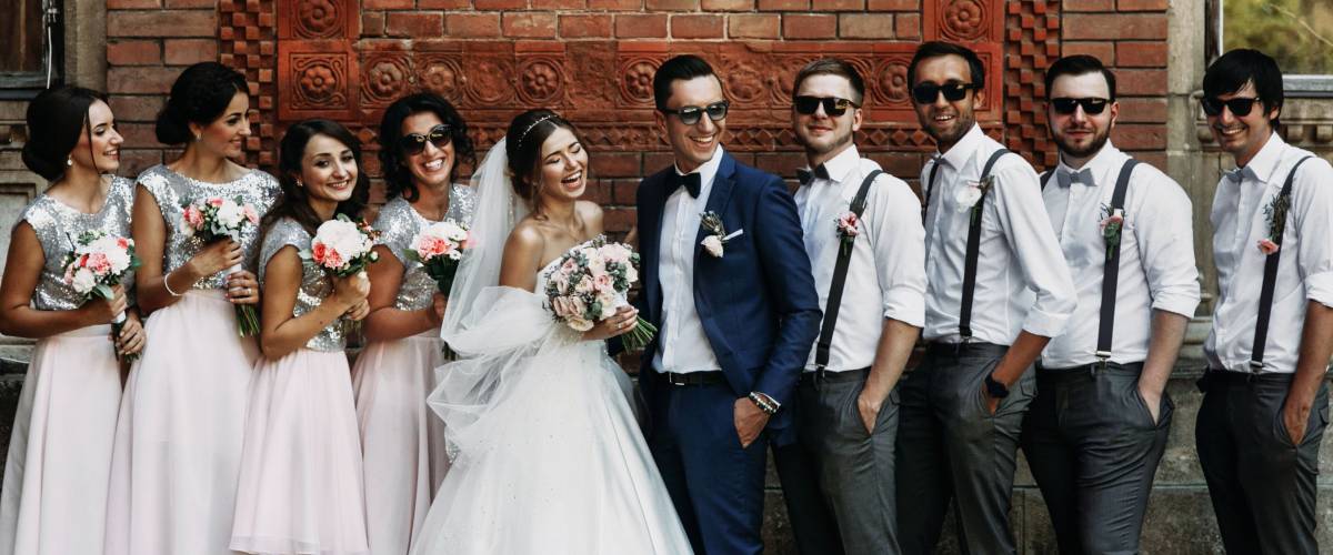 Cheerful & fun groom with bride, bridesmaids & groomsmen posing outdoors