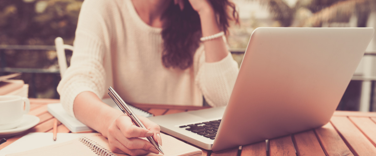Writing on a notepad with a laptop nearby