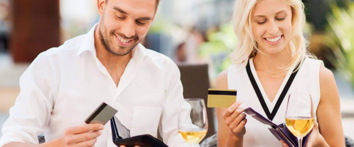 date, people, payment and financial independence concept - happy couple with credit cards in wallets and wine glasses paying bill at restaurant