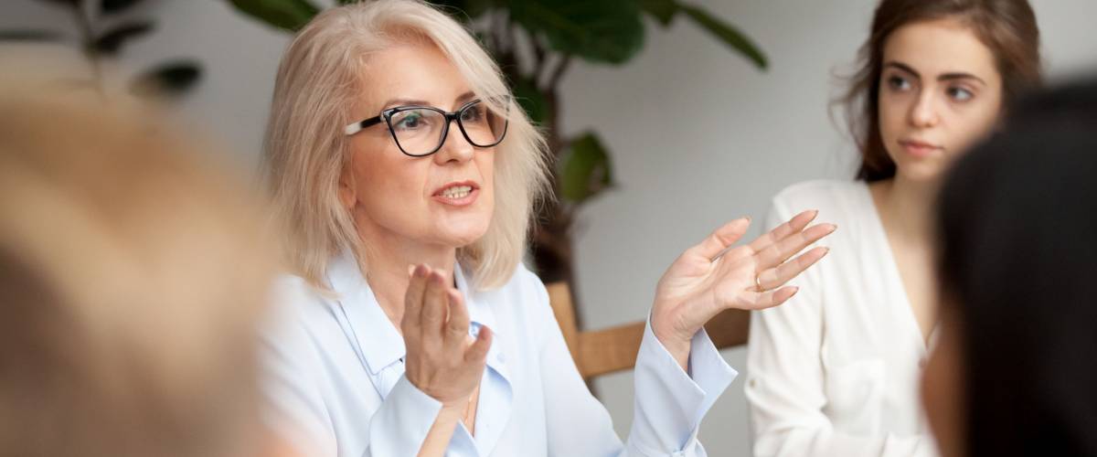 Attractive aged businesswoman, teacher or mentor coach speaking to young people