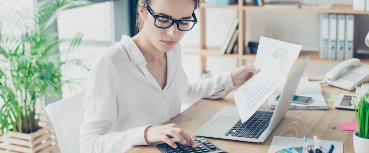 Successful business woman economist in formal wear, sitting at her work place in a light modern design office, making report, in front of laptop, so stylish, concentrated and thoughtful