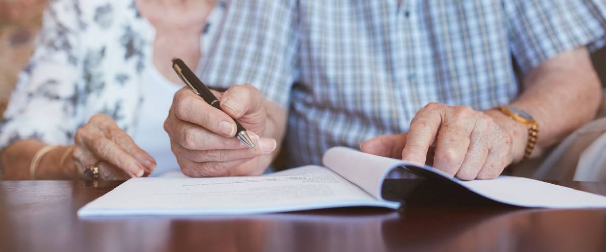 Senior couple signing will documents. Elderly caucasian man and woman sitting at home and signing some paperwork, focus on hands.