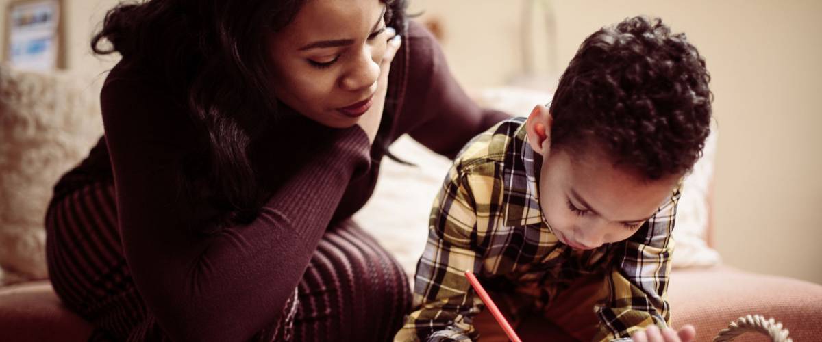 African American boy drawing at home with his mother.