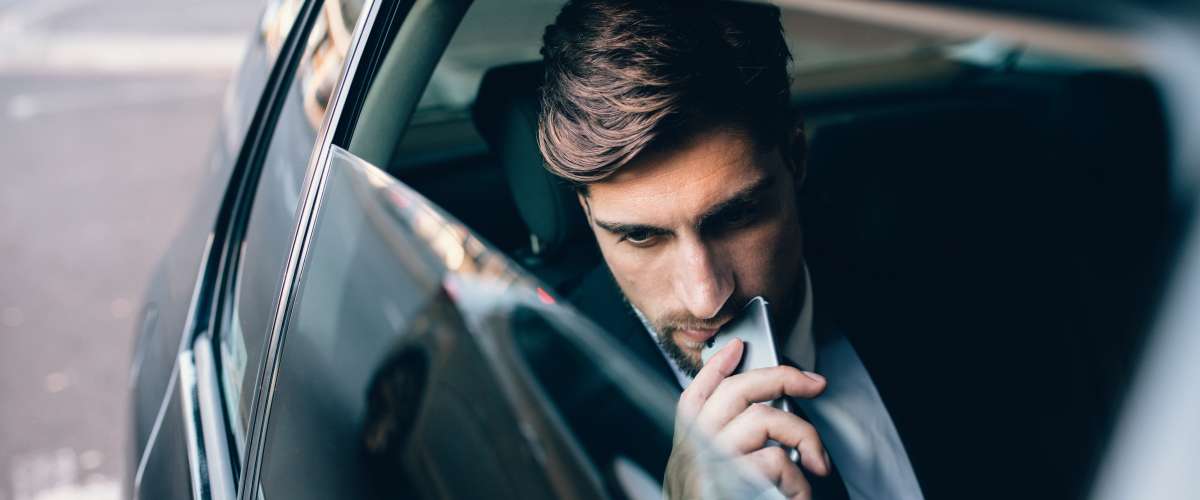 pensive young man in the back of a car holding a mobile phone