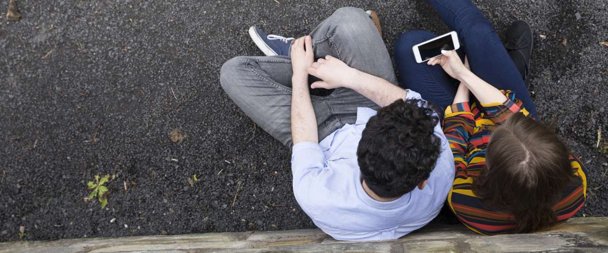 high angle couple sitting outdoors holding smartphone
