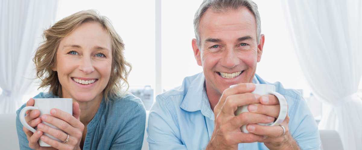 middle aged couple sitting on couch drinking coffee
