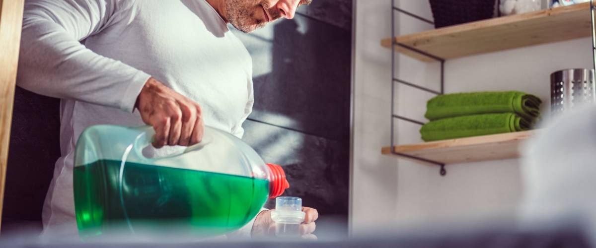 Man wearing white shirt pouring liquid laundry detergent In the bottle cap at laundry room