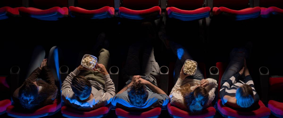 Young people sitting at the cinema, watching a movie and eating pop corn, top view