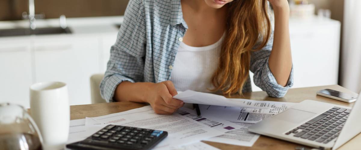 Indoor shot of casually dressed young woman holding papers in her hands, trying to save some money to repay her debts