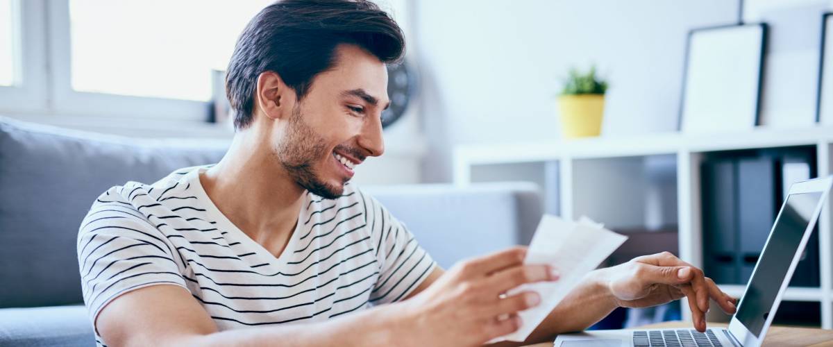 Happy man paying bills on his laptop in living room