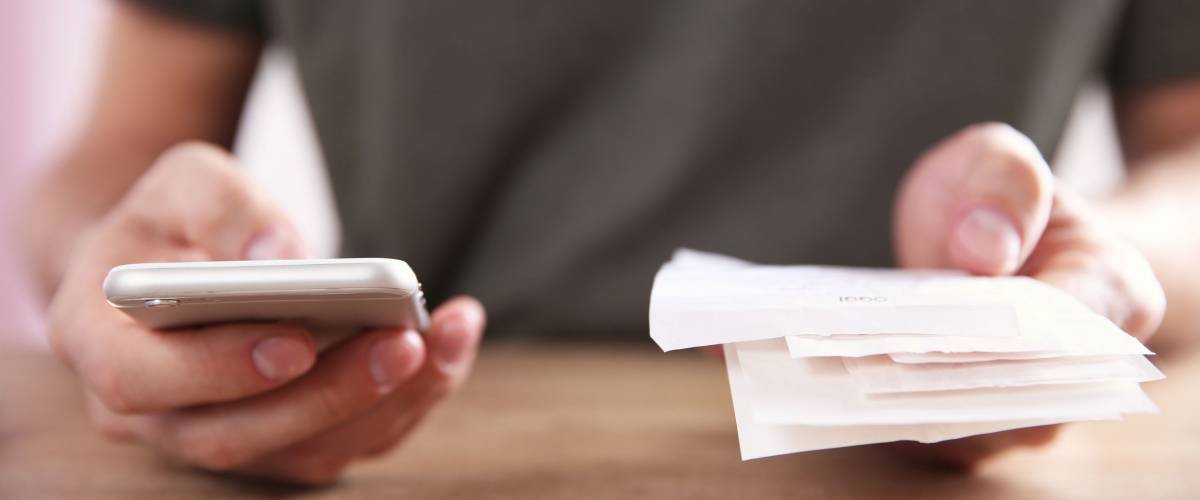 man using his phone and holding receipts
