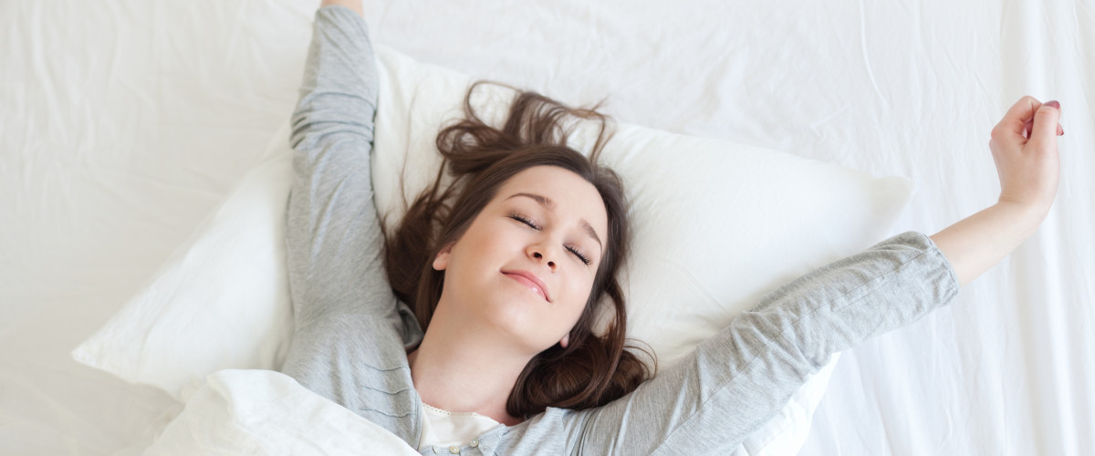 Woman waking up well rested on a white mattress