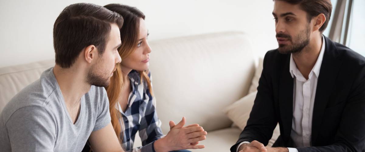 Millennial couple meet with realtor or broker talking about home purchase, husband and wife visit agent discussing buying house together or taking loan for first apartment, family counselling
