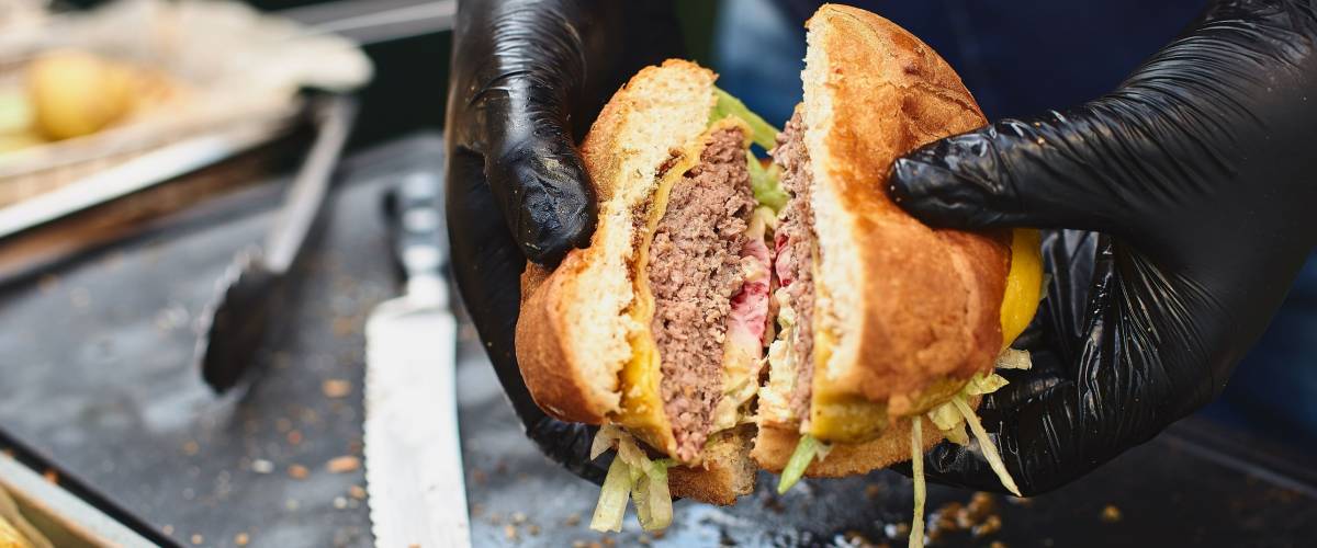 Close up of appetising beef burger. Chef's hands divide into half cooked hamburgers from beef. Street food ready to serve on a food stall. Chef cooks an American tasty hamburger.
