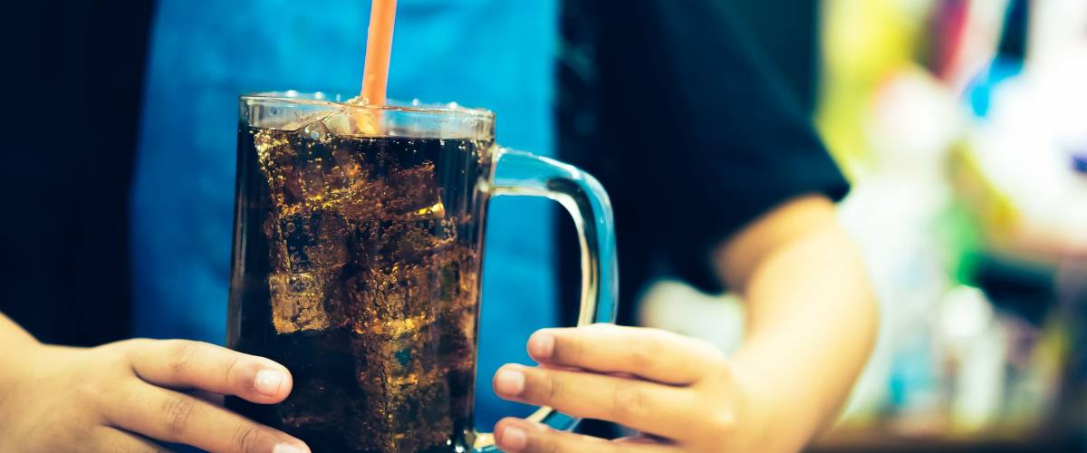 Glass of soda waters or is a sweetened and carbonated drink, which including of caffeine. Side view of refreshing soda with bubbles and ice on top.