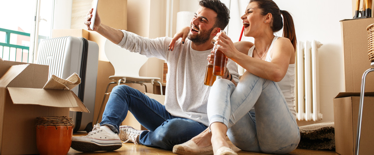 Young couple moving in new home. Sitting on floor and relaxing after cleaning and unpacking. Taking selfie with tablet.