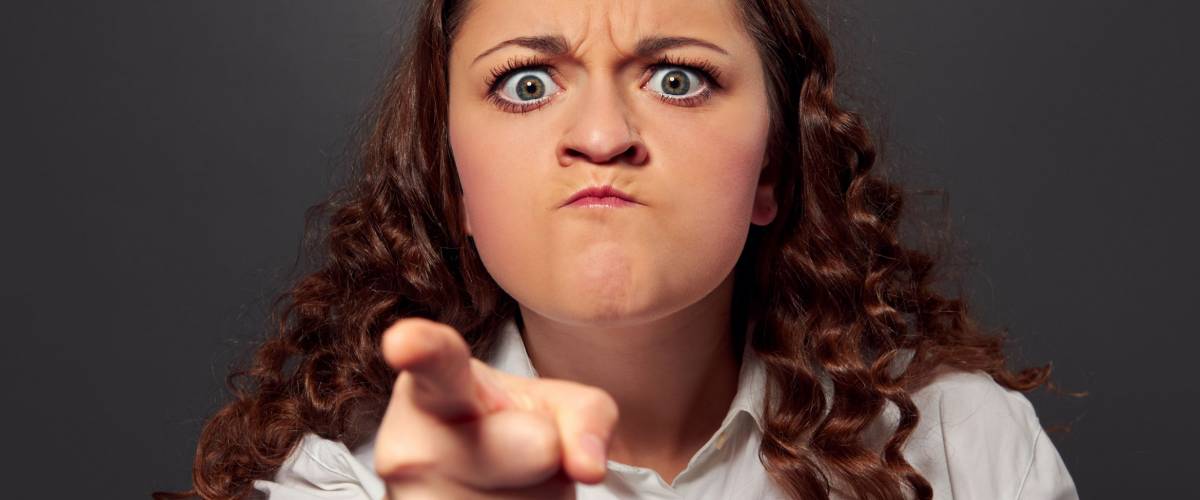 angry young woman pointing at camera over grey background