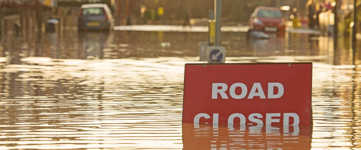 A 'Road Closed' sign partially covered in flood water