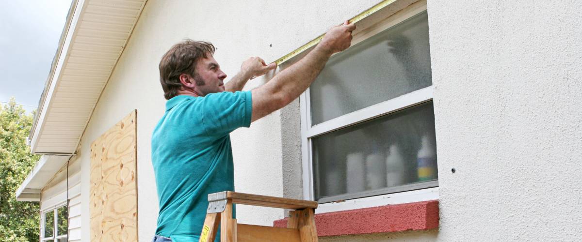 A man measuring windows for hurricane shutters or plywood.