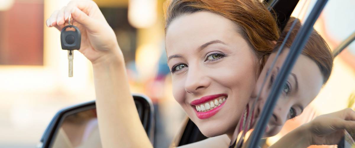 Closeup portrait happy, smiling, young attractive woman, buyer sitting in her new blue car showing keys isolated outside dealer