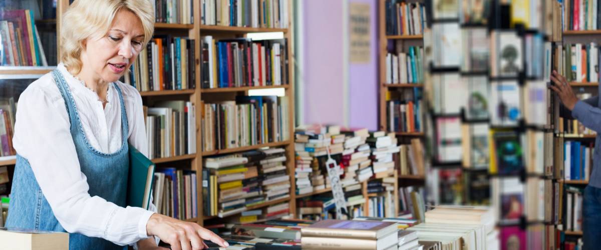 Positive mature cheerful woman searching for new book on shelves in book store