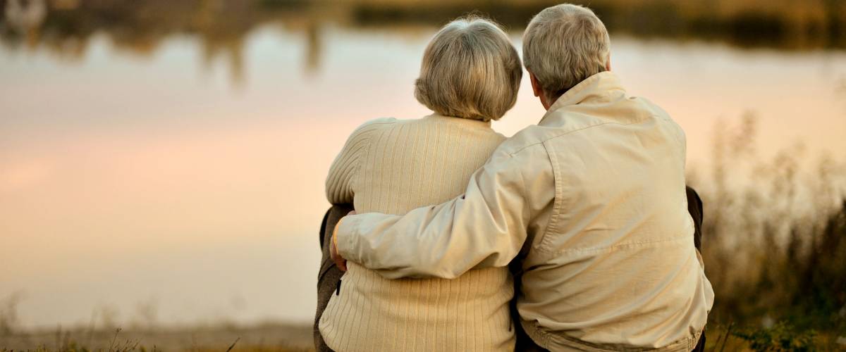 Happy senior couple sitting in summer near lake during sunset