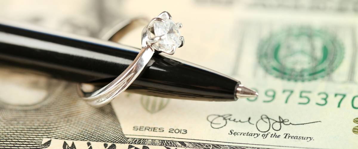 Wedding ring on pen, on banknotes background