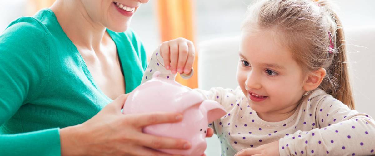 Mother and daughter putting coins into piggy bank