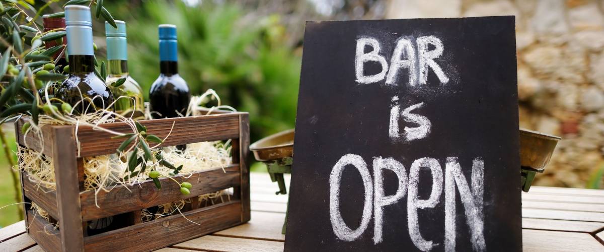 Bar is open sign and vintage wooden crate full of wine bottles decorated with olive branches on a table