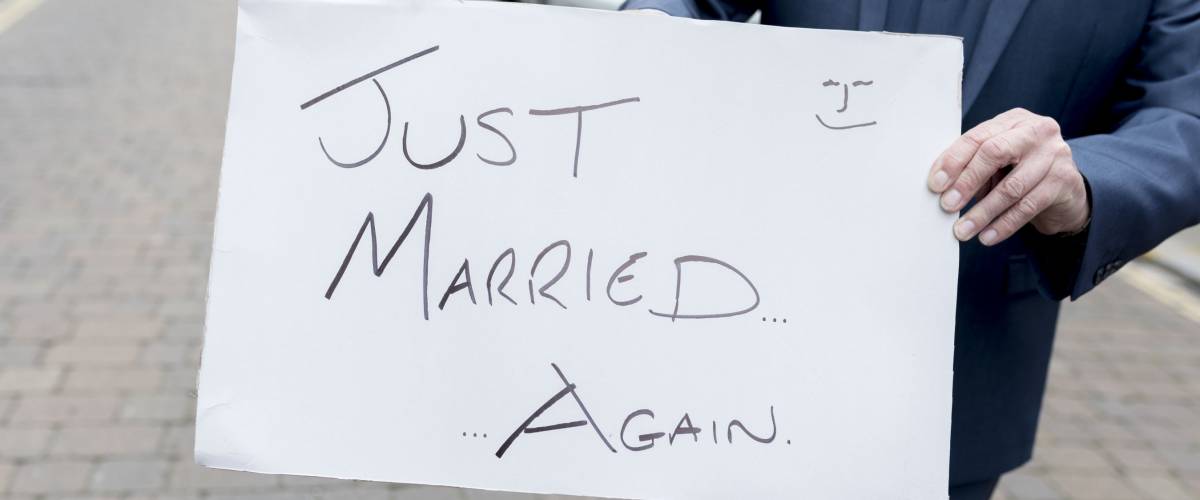 Best man or groom holding a homourous hand written sign stating Just married...again at a second wedding or renewal of vows in the UK