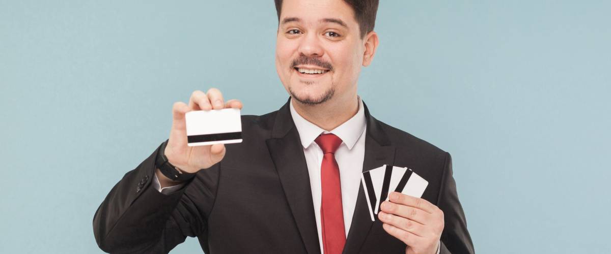 Happiness business man holding many cards. One bank card will replace all your cards. Indoor, studio shot, isolated on light blue or gray background