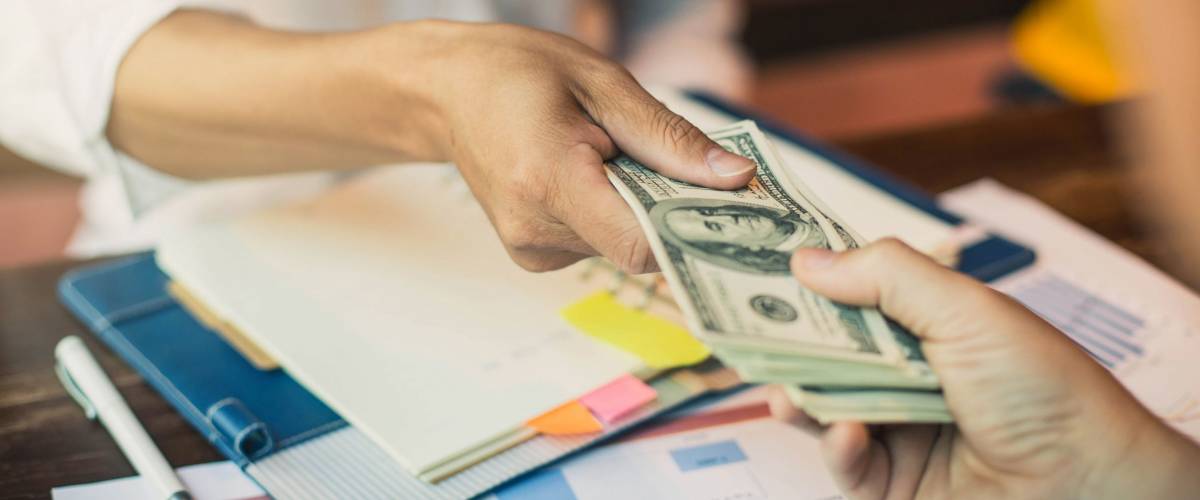 Man offering batch of hundred dollar bills. Hands close up. Hand giving money - United States Dollars (or USD).