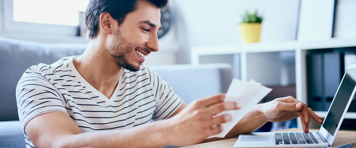 Happy man paying bills on his laptop in living room