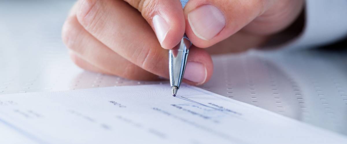 A Male Hand Filling Out The Amount On A Cheque