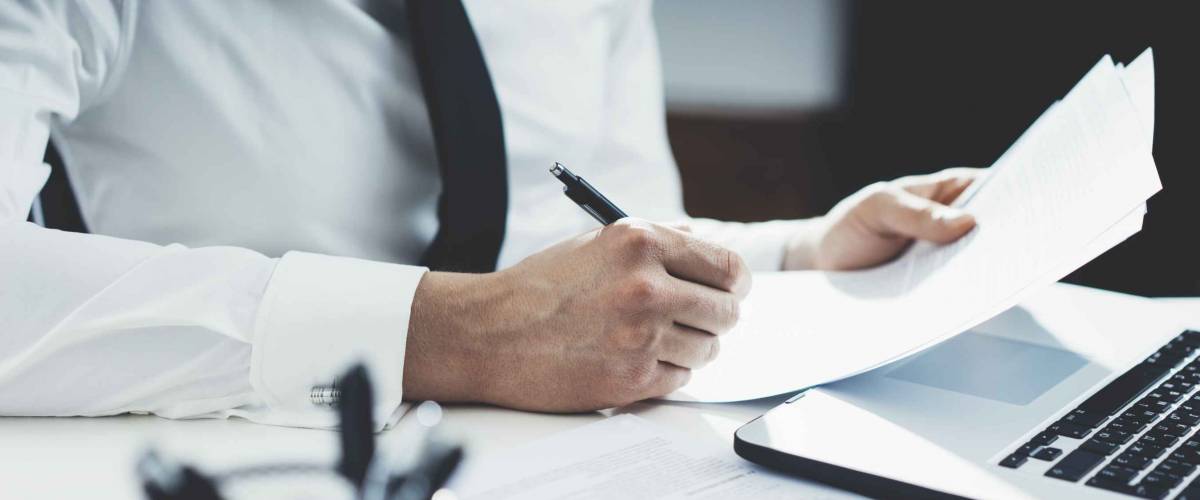 Professional banker working at his office with documents and using modern laptop computer, close-up of male hands signing contract