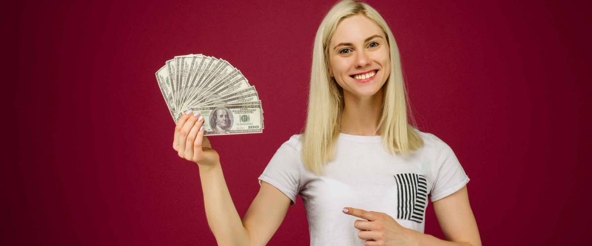 Young woman pointing towards a stack of money with her finger isolated on ruby background - Image