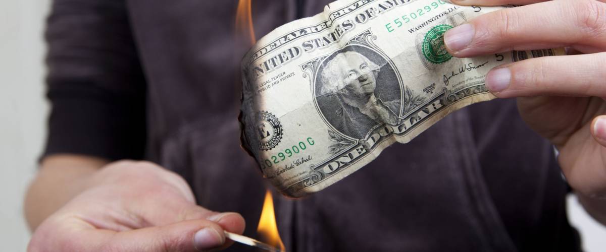 Hands setting fire to a dollar bill