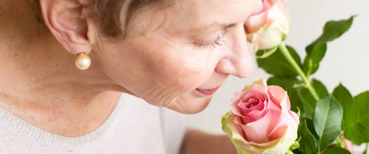 Older woman in beige top smelling pink rose (selective focus and close up)