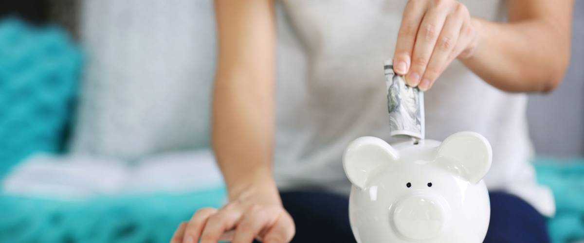 Female hand putting money into piggy bank and counting on calculator closeup