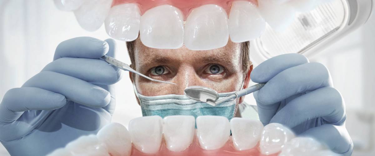 Stomatology. Dentist over open patient's mouth looking in teeth. Inside vew