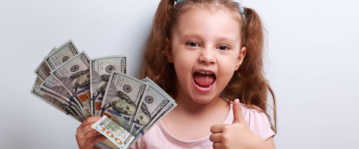 Happy enjoying kid girl holding money and showing thumb up sign on blue background