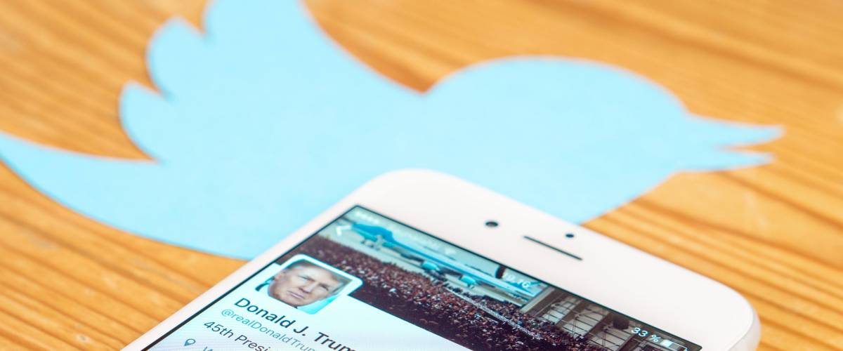Twitter symbol on table, with smartphone showing Donald Trump Twitter feed