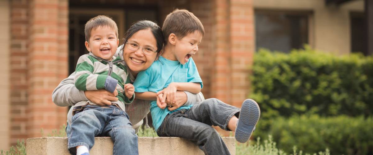 Mixed race children with their Asian mother play in front of their family home. Image captures family love, confidence, cheerfulness, and togetherness at home.