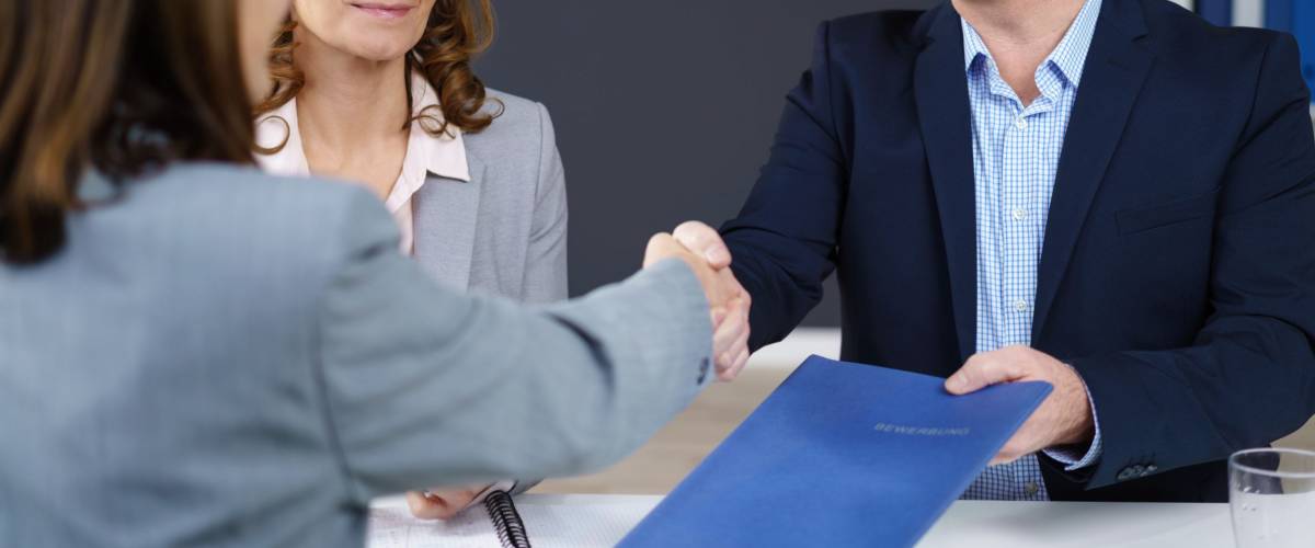 Businessman and woman conducting an interview smiling as they congratulate and shake hands with the prospective applicant while holding her CV