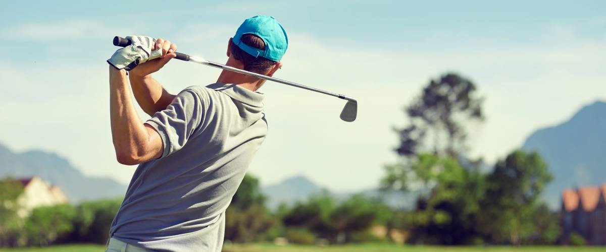 Golfer hitting golf shot with club on course while on summer vacation