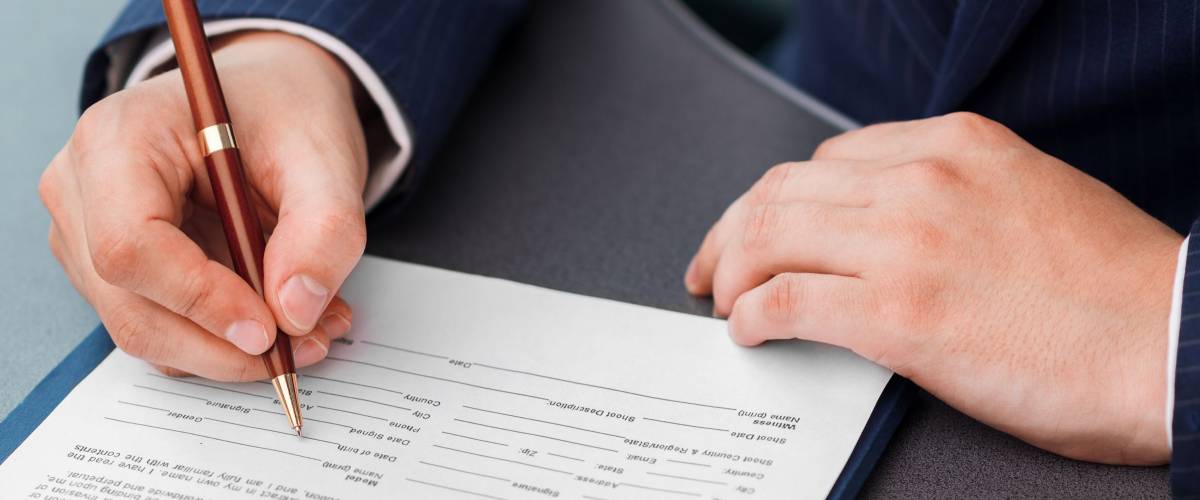 Close-up of businessman hands with pen signing financial document lying on the desk.