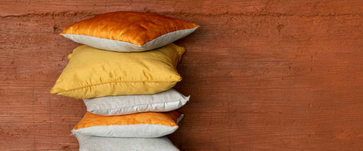 Orange and yellow pillows stack on terracotta background. Different shades of yellow, terracotta and orange bed linen decorative cushions. Pile concept.