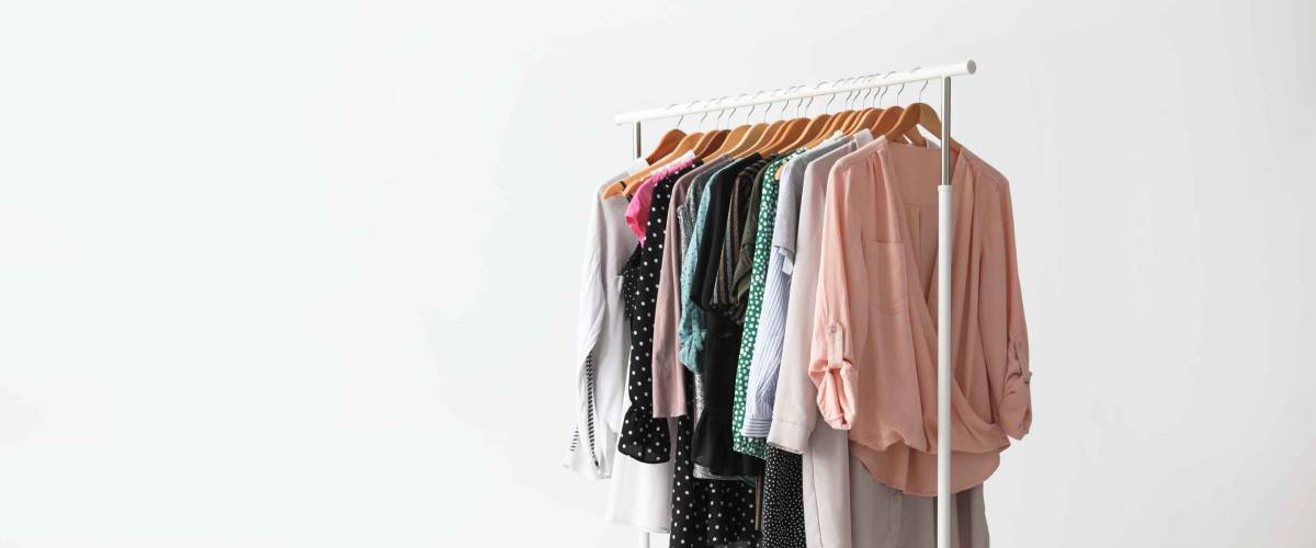 Wardrobe rack with stylish clothes near white wall indoors. Space for text