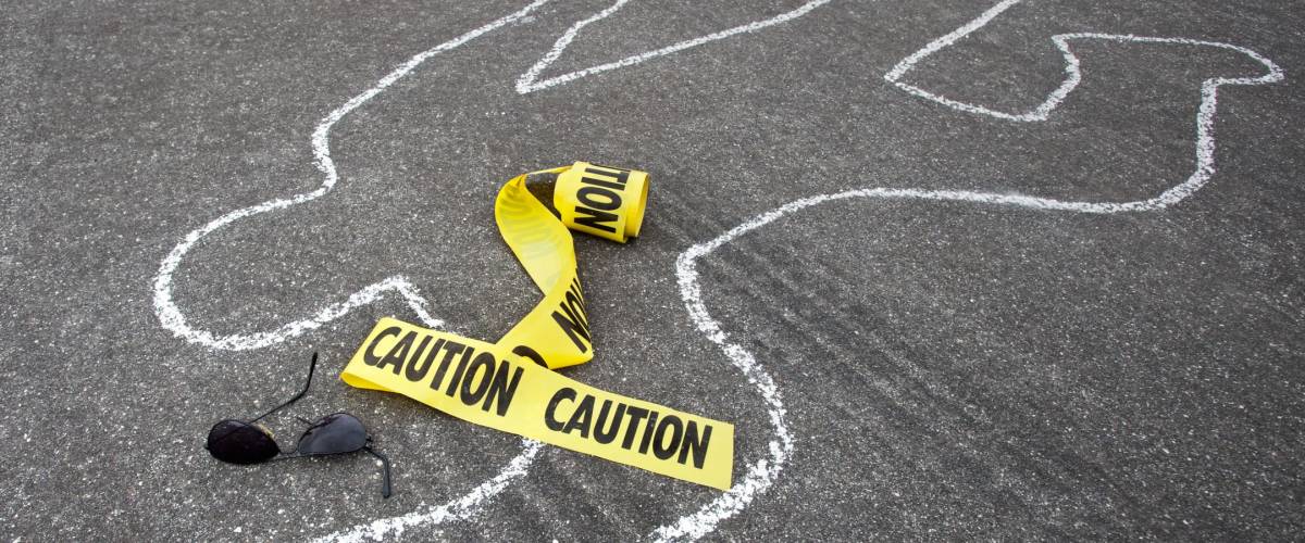 Caution tape and broken sun glasses rest near a chalk line from an auto accident.